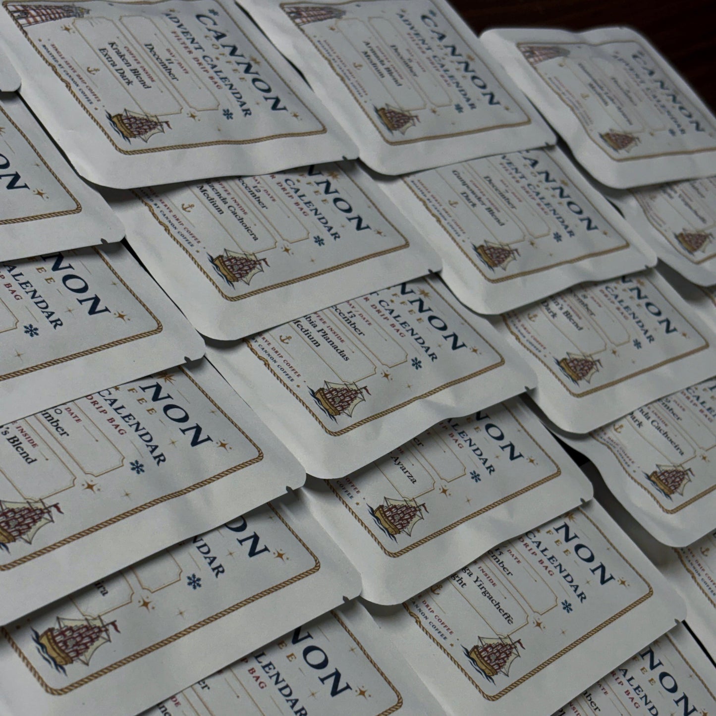 A stack of small white rectangular product packets with rounded corners, each printed with the brand name NON and the words calendar and a small illustrated ship, arranged overlapping on a dark surface.