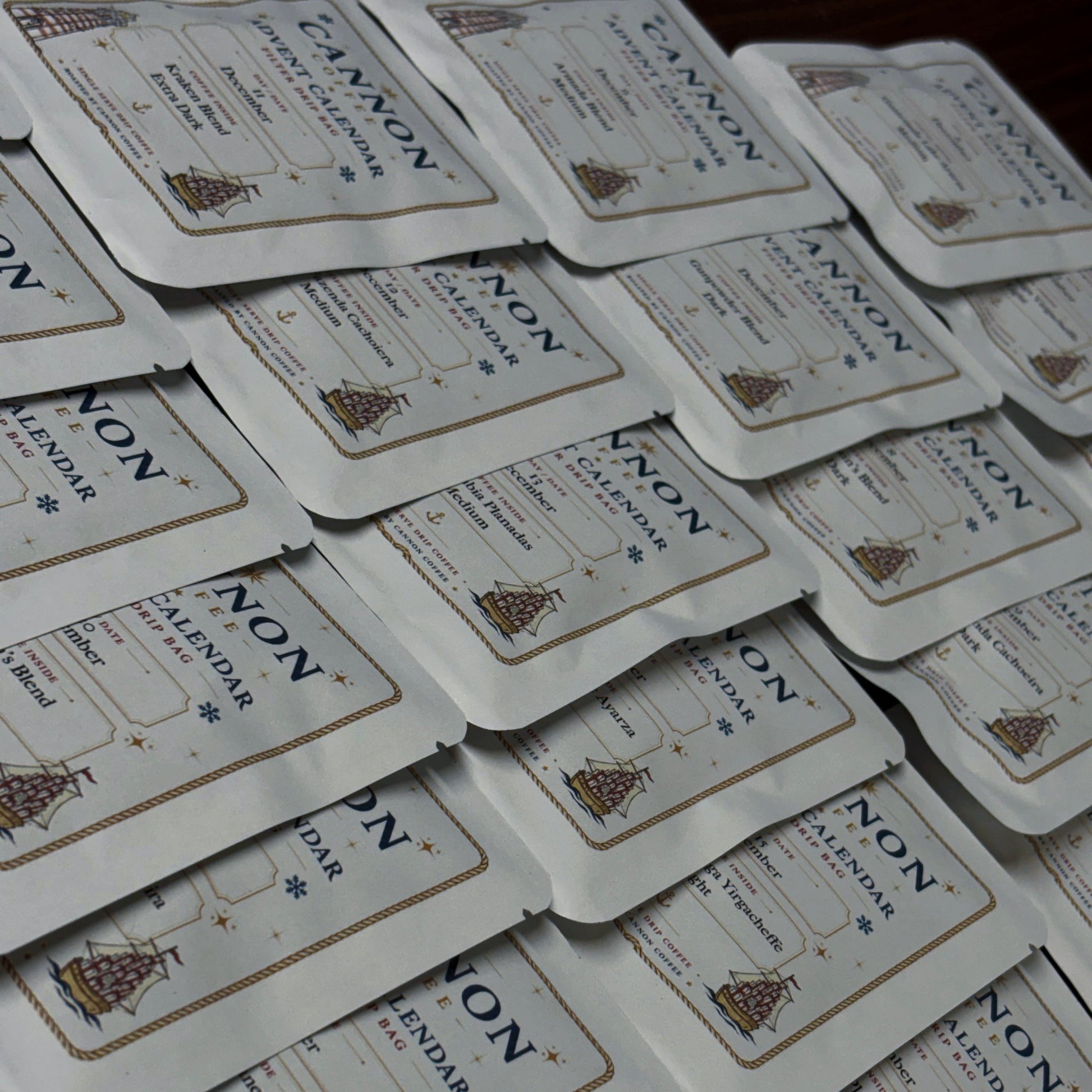 A stack of small white rectangular product packets with rounded corners, each printed with the brand name NON and the words calendar and a small illustrated ship, arranged overlapping on a dark surface.