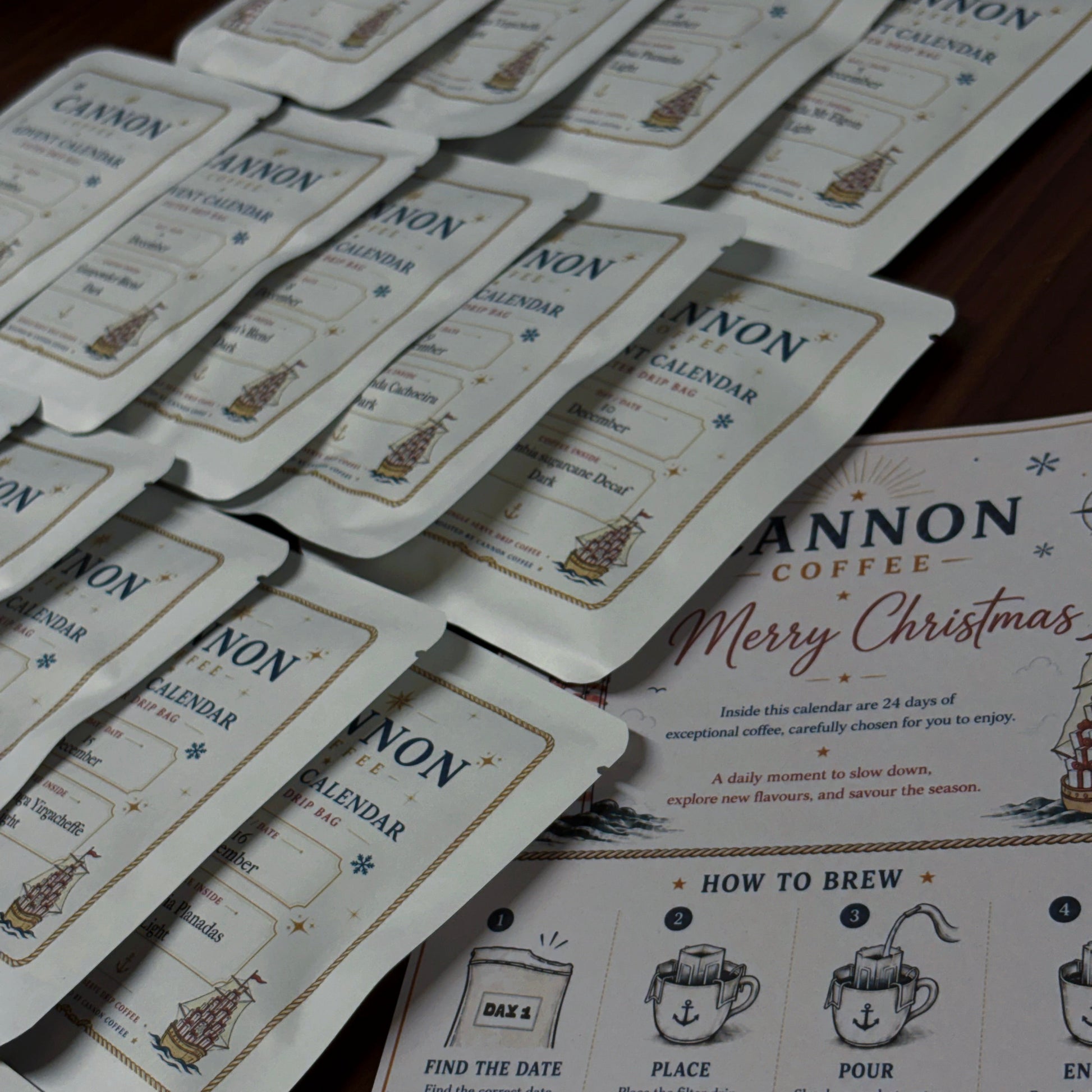 A set of Cannon Coffee Christmas calendar sachets arranged on a dark wooden surface next to a printed 'How to Brew' guide and a Christmas-themed card.