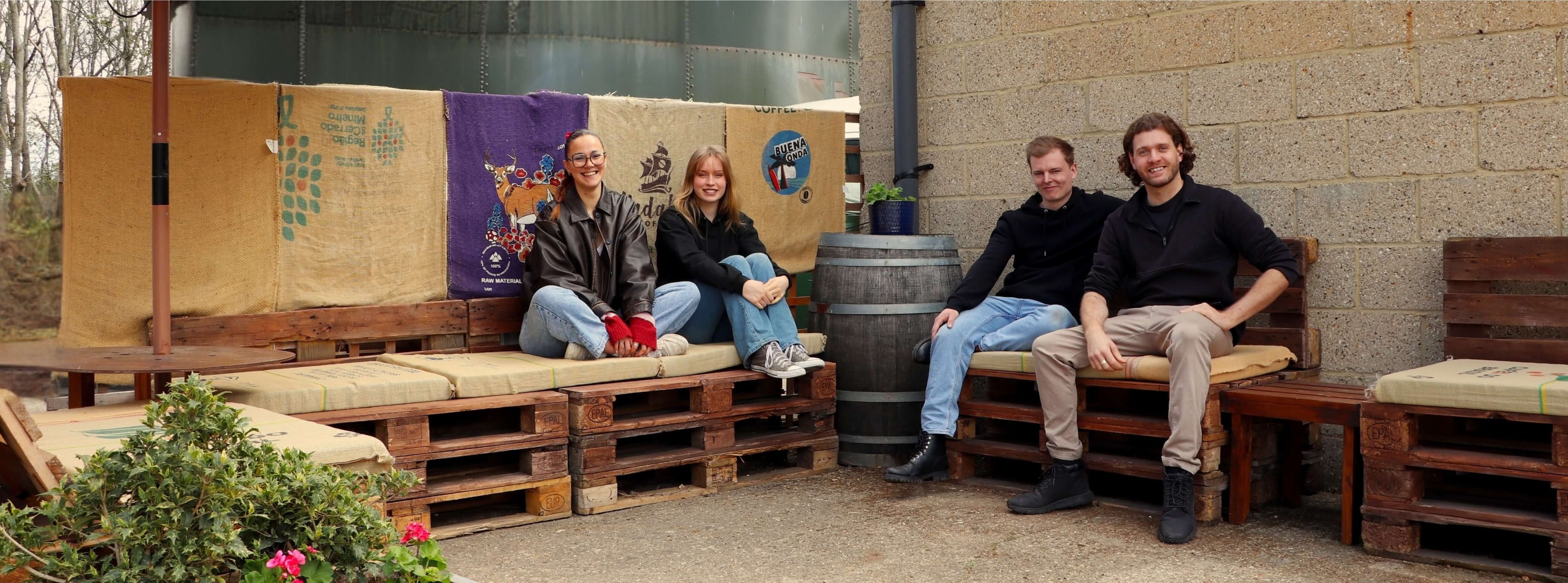 Four people sitting on a wooden bench made from pallets in an outdoor setting.