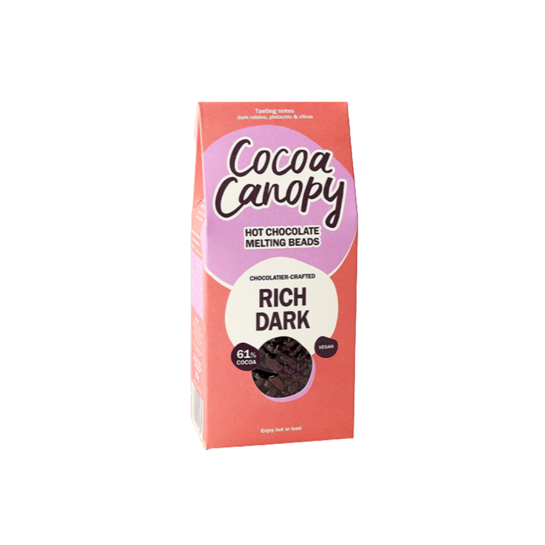 A package of Cocoa Canopy Rich Dark hot chocolate melting beads, featuring a coral pink box with a purple and white label design.